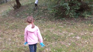 Dziewczynka chodzi po trawie i szuka śmieci a w tle drzewa