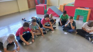 Dzieci siedzą w klasie na podłodze w kole, piszą na kartkach