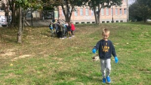 Chłopiec idzie po trawie i niesie śmieć na tle budynku i grupki dzieci
