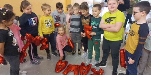 Uczniowie stoją za ułożonym na podłodze z czerwonych balonów napisem kawa