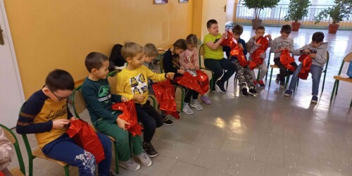 Dzieci siedzą na krzesełkach z czerwonymi balonami w dłoniach