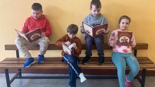 Dzieci czytają książki. Siedzą na ławkach na korytarzu szkolnym