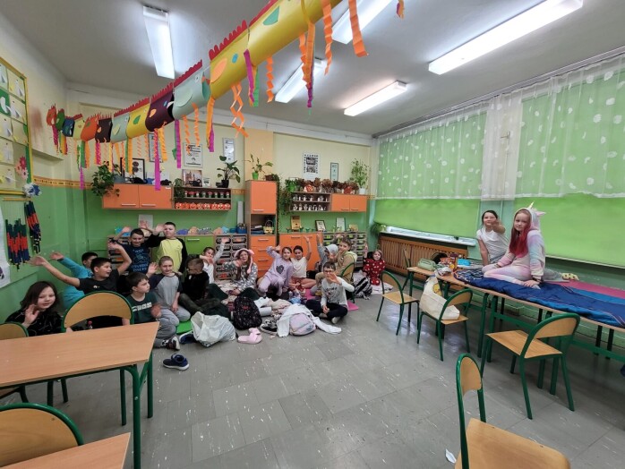 Uczniowie w piżamach siedzą na podłodze z karimatami i poduszkami
