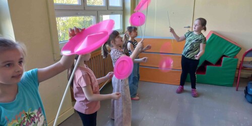 Dziewczynki żonglują kolorowymi talerzykami. Próbują nimi kręcić w jedną stronę
