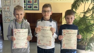 Zdjęcie przestawia zbliżenie na trzech uśmiechniętych chłopców z klasy 1, 2 i 3 z SP 45 . Trzymają w rękach dyplomy oraz nagrody wygrane w konkursie.